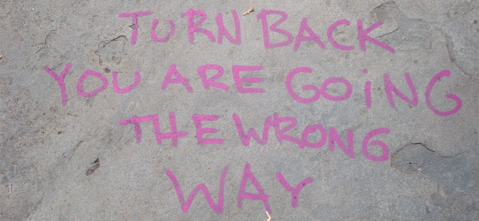 Photo of message written on sidewalk. The message says, Turn Back. You are going the wrong way.